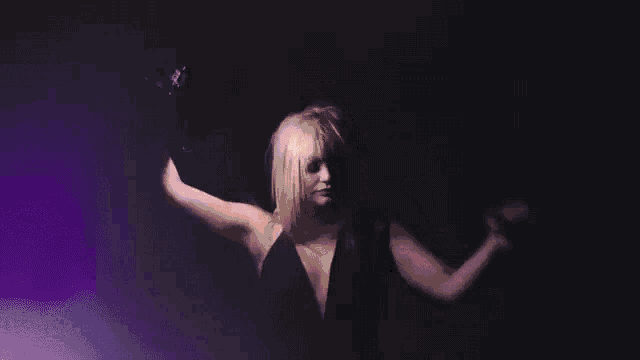 a woman is dancing in a dark room with her arms outstretched in the air .