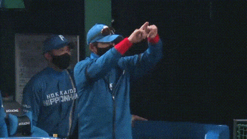 a man in a blue hokkaido nipponham jacket is standing with his arms outstretched .