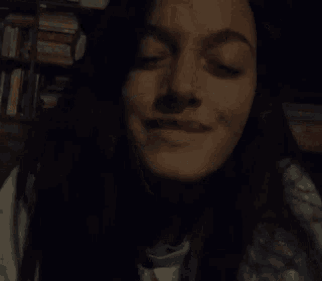 a close up of a woman laughing with her eyes closed in front of a bookshelf .