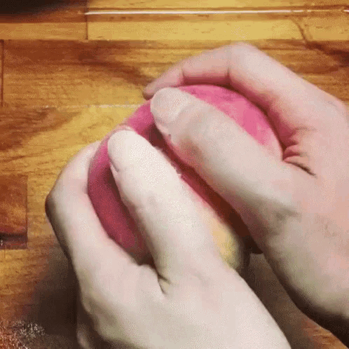 a person is peeling a pink peach with their hands