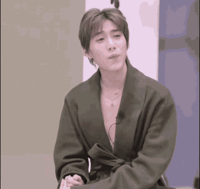 a young man wearing a green coat and a necklace looks at the camera