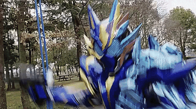 a blue and gold robot is fighting another robot in a park with trees in the background .