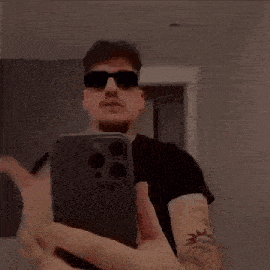 a man wearing sunglasses is taking a selfie with his mouth open while holding a cell phone .