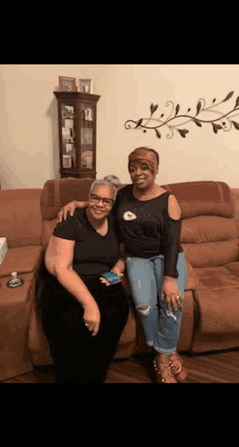 two women are posing for a picture while sitting on a couch in a living room .