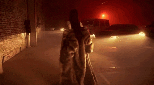 a woman is walking down a street at night with a van in the background
