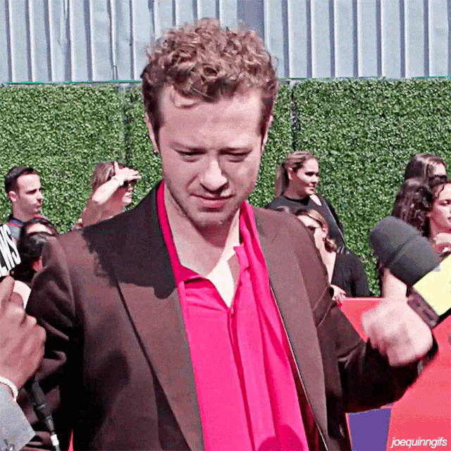 a man wearing a red shirt and a brown suit is being interviewed by a reporter