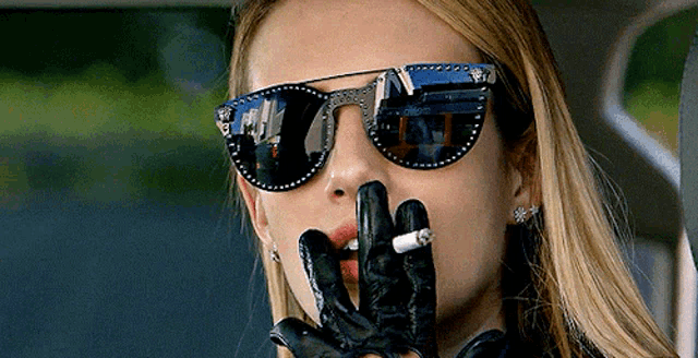 a woman wearing sunglasses and leather gloves is smoking a cigarette