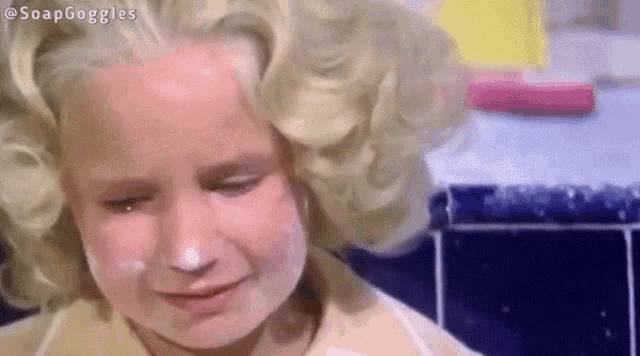 a little girl with soap on her face is crying in a bathroom .