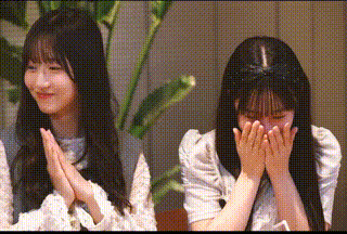 two girls with long hair are sitting next to each other with their hands on their faces .