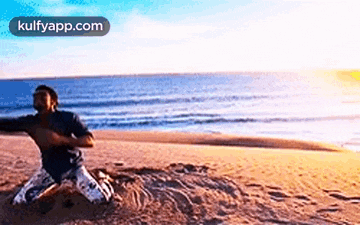 a man is kneeling in the sand on a beach with the ocean in the background .