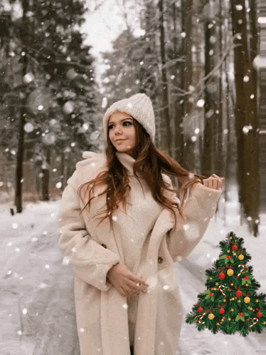 a woman in a white coat and hat is standing in the snow next to a christmas tree
