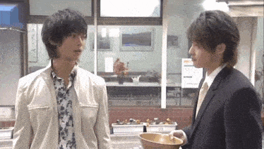 two men are standing next to each other in a room and one is holding a bowl