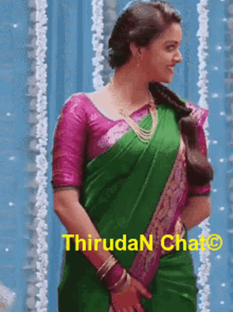 a woman in a green saree and a pink blouse is standing in front of a blue curtain .