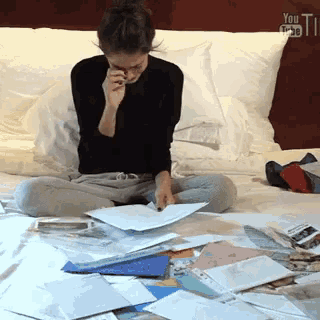 a woman sits on a bed with a bunch of papers and a youtube logo