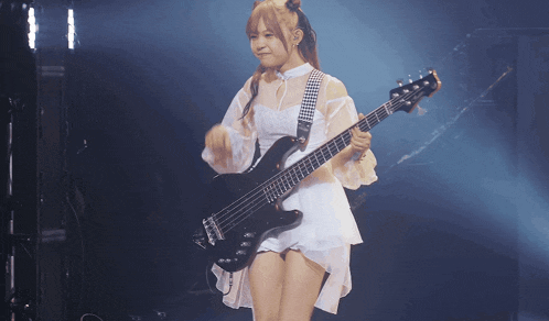 a woman in a white dress is holding a black bass guitar