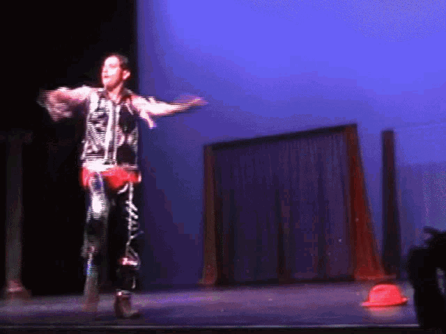 a man stands on a stage with his arms outstretched in front of a blue curtain