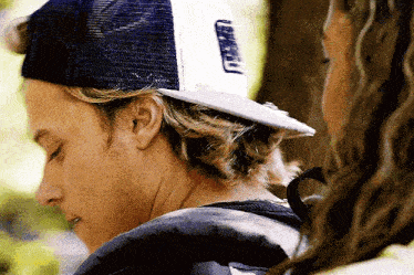 a man wearing a trucker hat is looking at a woman .