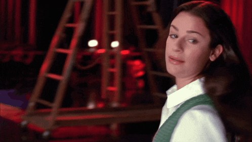 a woman in a white shirt and green vest is looking at the camera
