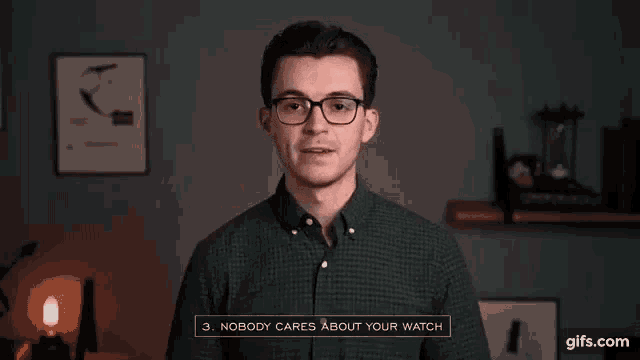 a man wearing glasses and a green plaid shirt is standing in front of a wall .