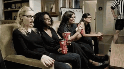 a group of women are sitting on a couch holding cups of coffee and drinks .