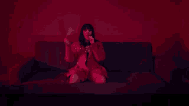 a woman in a red dress is sitting on a couch in a dark room with a red light behind her .
