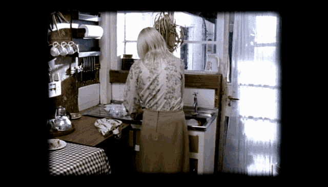 a woman is washing dishes in a kitchen with a checkered tablecloth