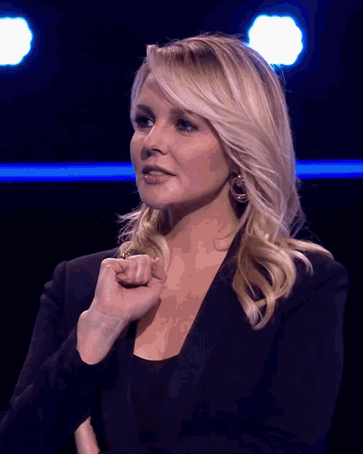 a woman in a black jacket holds her fist up in front of her face