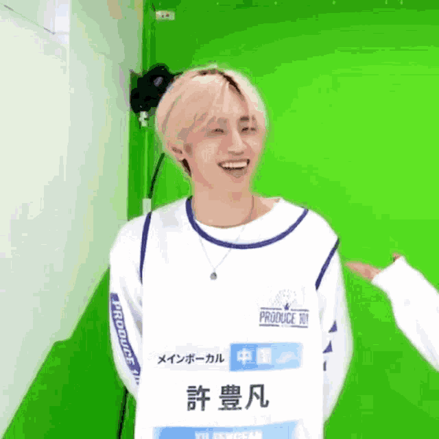 a young man is smiling in front of a green screen while wearing a white and blue sweater .