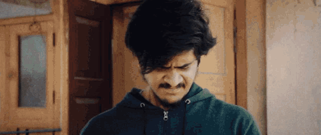 a man with a beard is wearing a green hoodie and making a face .