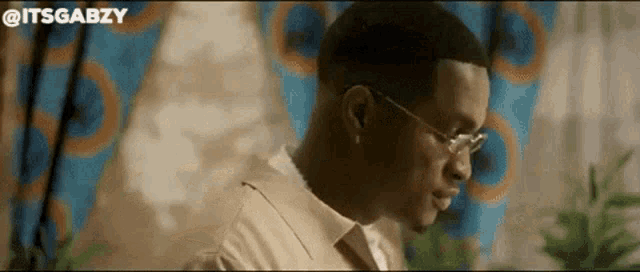 a man wearing glasses and a white shirt is sitting in front of a curtain .