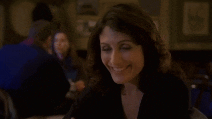 a woman is smiling while sitting at a table in a restaurant with her hand on her chin .