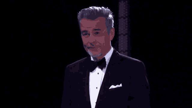 a man in a tuxedo with a bow tie is standing in front of a black background .