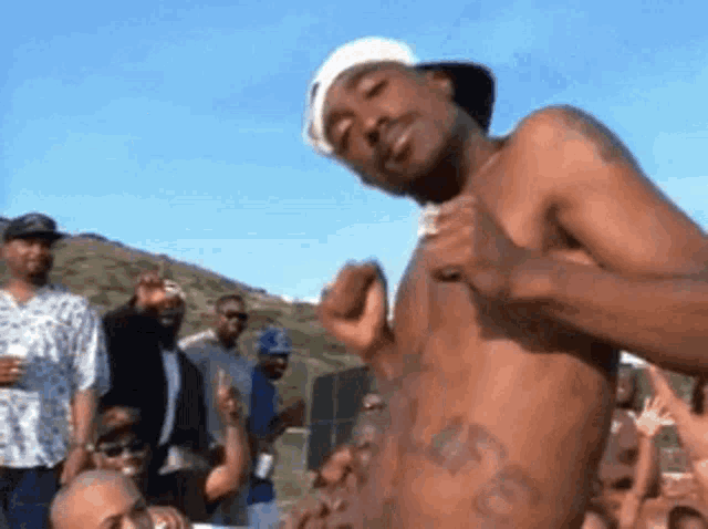 a shirtless man with a tattoo on his stomach is standing in front of a crowd of men .