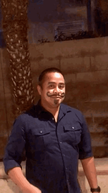 a man in a blue shirt has a fake mustache painted on his face