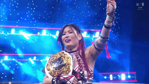 a female wrestler is holding a championship belt in front of a live audience