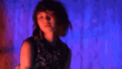 a woman in a sequined dress is standing in front of a blue curtain in a dark room .