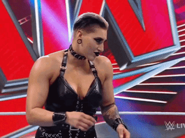 a woman in a black dress and choker is standing in a ring .