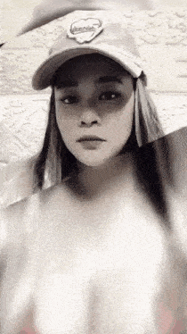 a woman wearing a hat and a white shirt is looking at the camera .