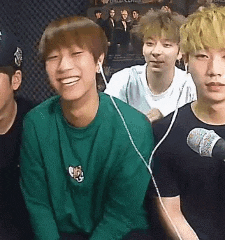 a group of young men are sitting in front of a microphone and smiling while wearing headphones .