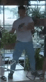 a man in a white shirt and blue jeans is standing in a room holding a camera .