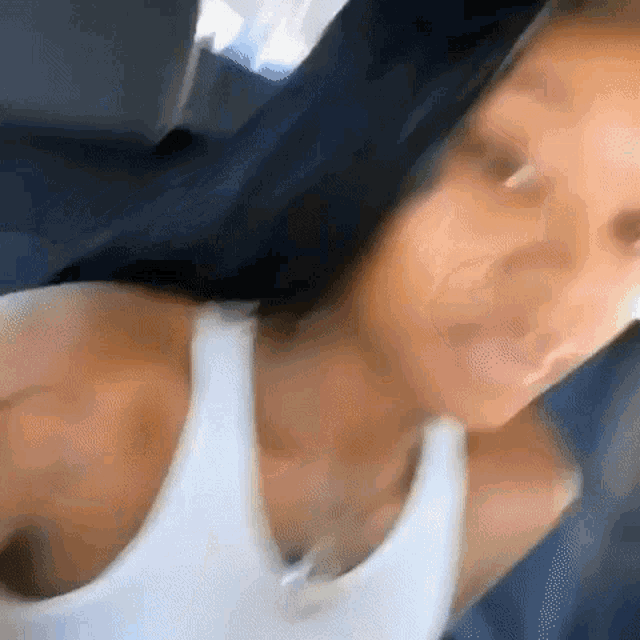 a woman is sitting in a car wearing a white tank top and taking a selfie .