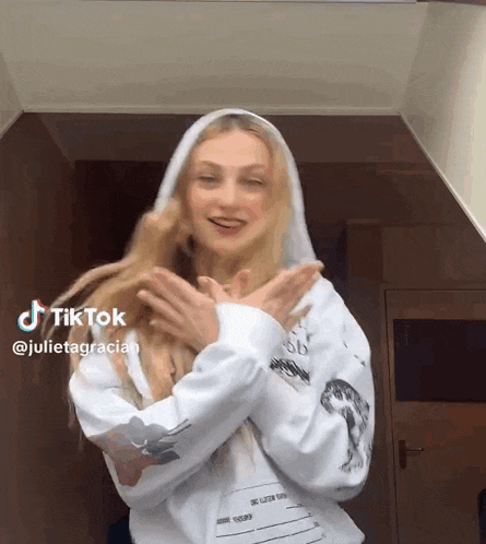 a woman wearing a white hoodie is making a tiktok with her hands outstretched