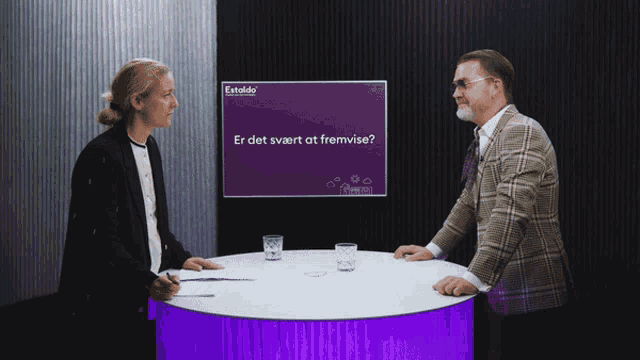 a man and a woman are sitting at a table in front of a screen that says " er det svært at fremtide "