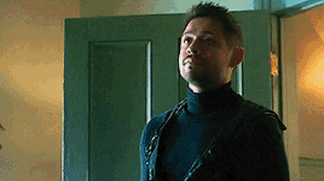 a man wearing a black turtleneck sweater is standing in front of a green door .