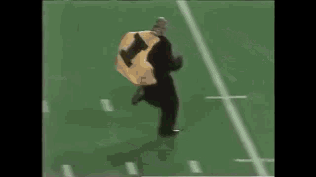 a man in a yellow jacket is running on a football field with the word winnipeg on it
