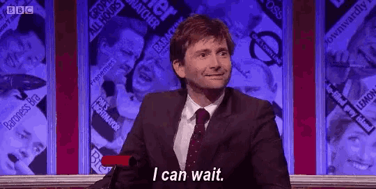 a man in a suit and tie is sitting in front of a screen and says `` i can wait '' .