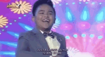 a young boy in a suit and bow tie is standing in front of a stage .