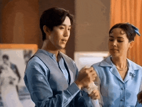 a man and a woman are standing next to each other in a room . the man is wearing a blue shirt .