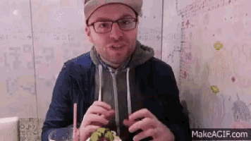 a man wearing glasses and a hat is eating food with a straw