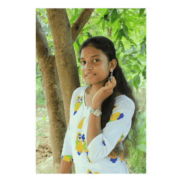 a girl wearing an owl shirt and a watch is standing in front of a tree